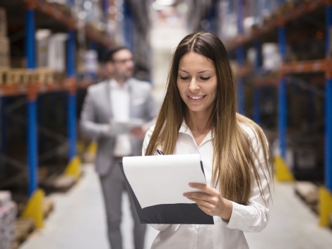 Portrait of gorgeous brunette woman manager controlling business in warehouse logistic center. Well dressed successful woman checking distribution while CEO walking behind her.